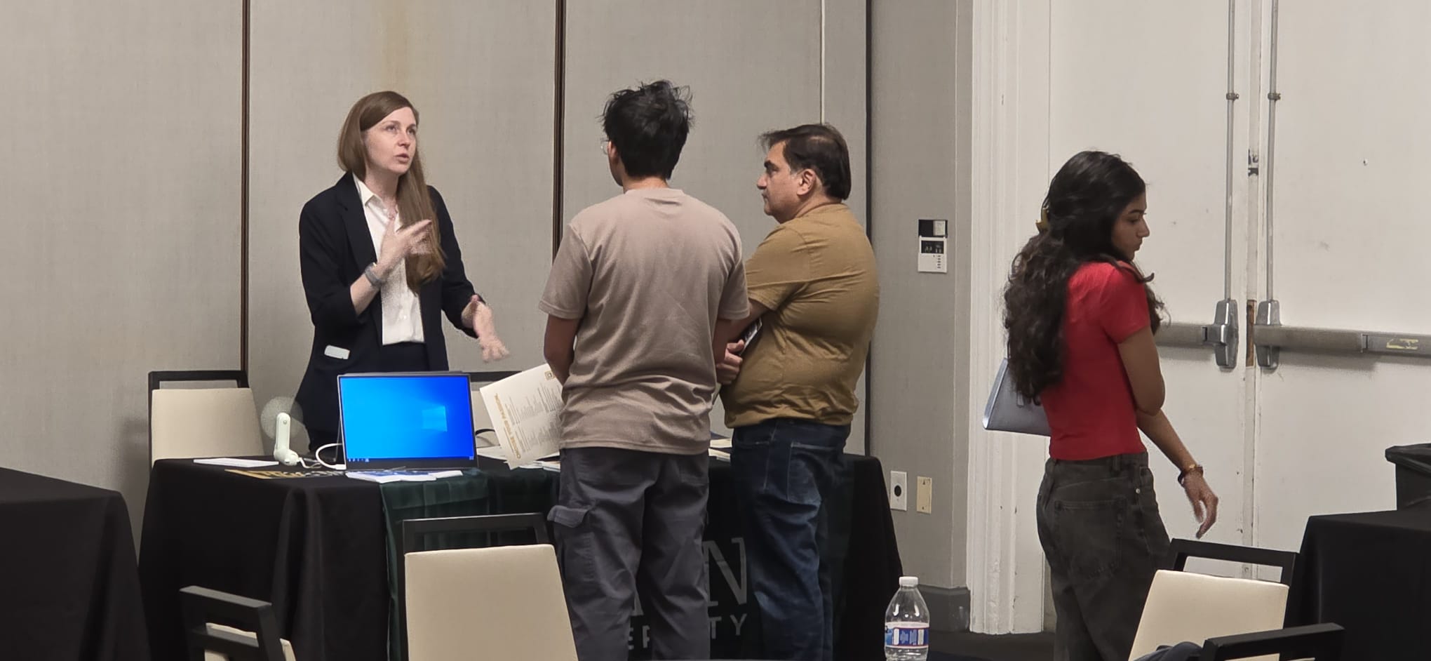 A Tiffin University representative speaking with attendees near a laptop and printed materials